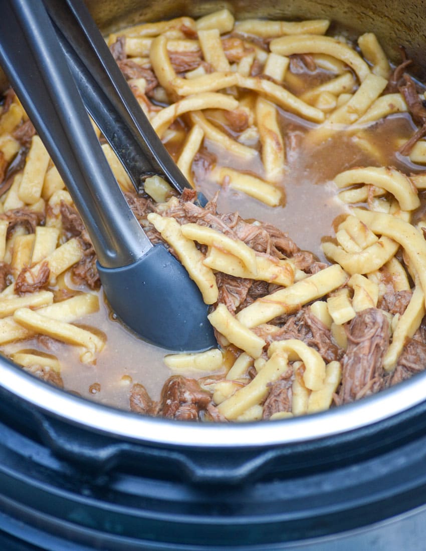 tongs in an instant pot filled with beef and egg noodles in broth