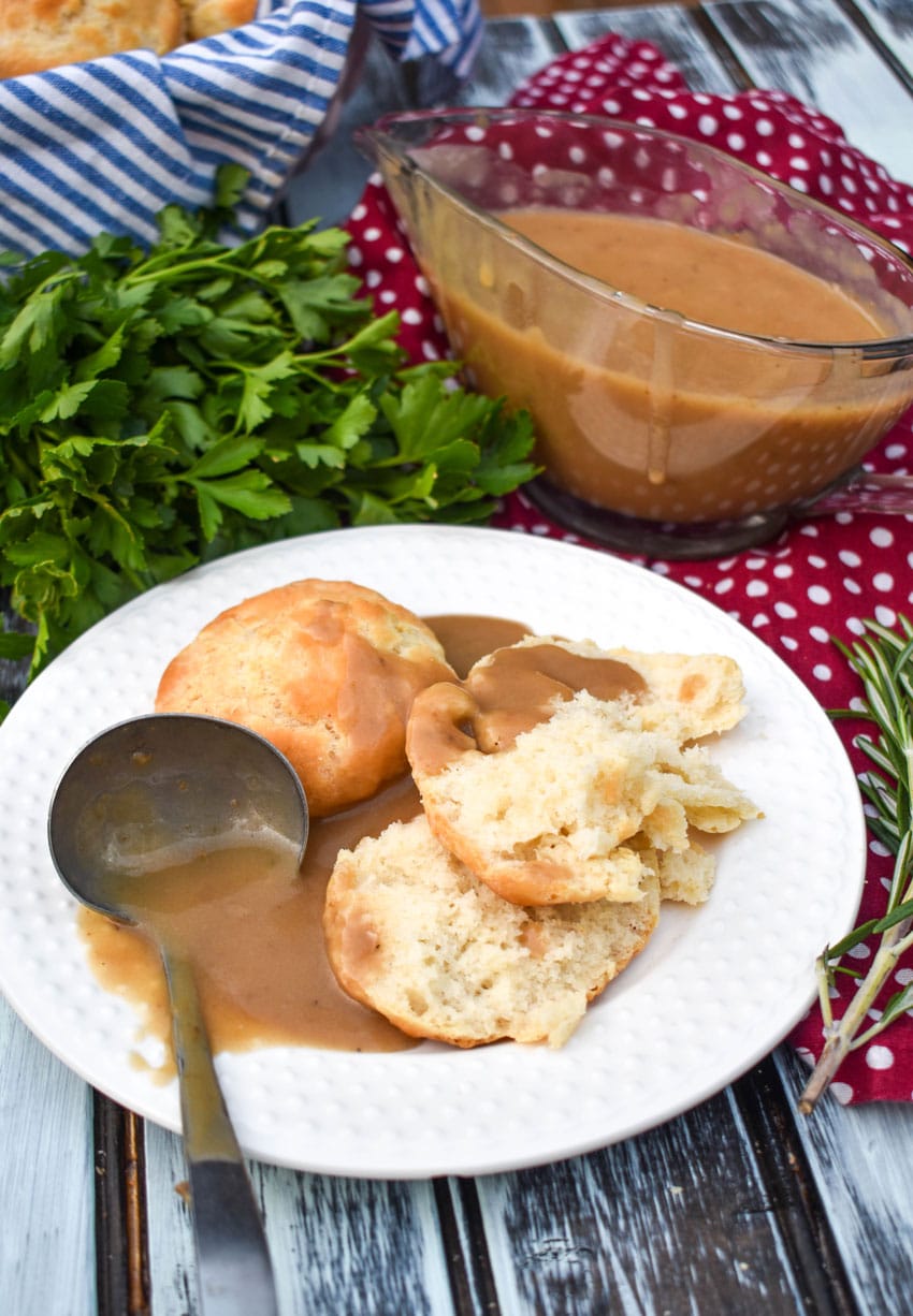 a gravy ladle on a white plate with make-ahead turkey gravy over biscuits