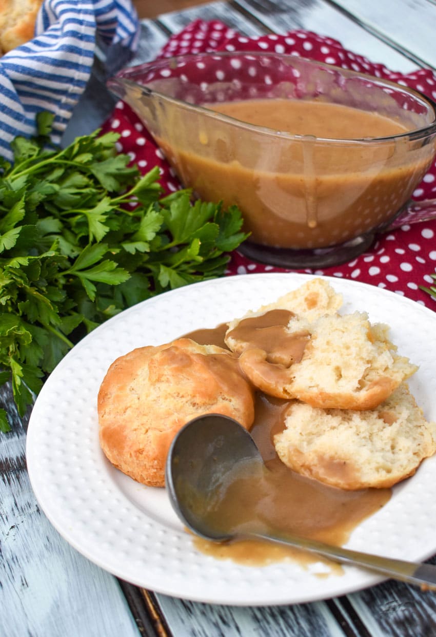 a gravy ladle on a white plate with make-ahead turkey gravy over biscuits