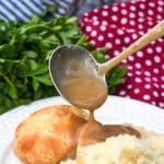 a gravy ladle pouring make ahead turkey gravy out over biscuits on a white plate