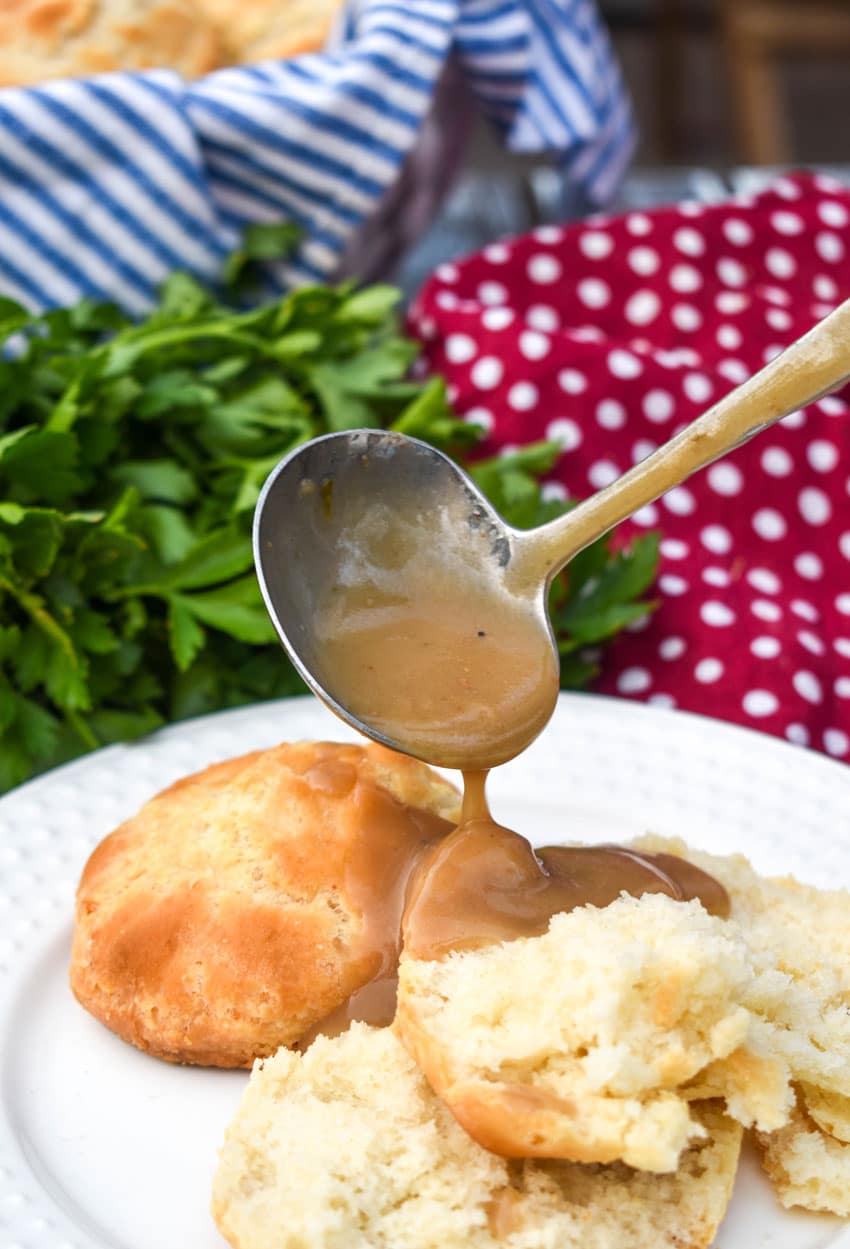 Make Ahead Turkey Gravy a gravy ladle pouring make ahead turkey gravy out over biscuits on a white plate