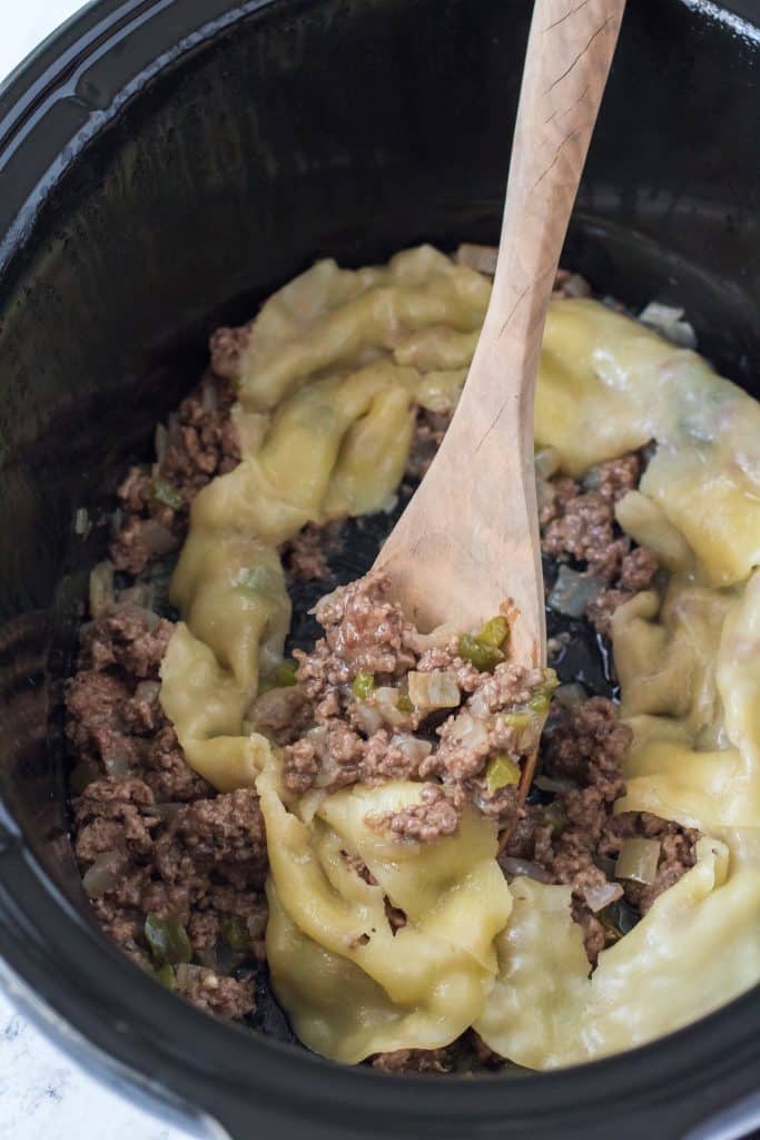 cooked ground beef with peppers and onions covered with melted cheese in a black slow cooker