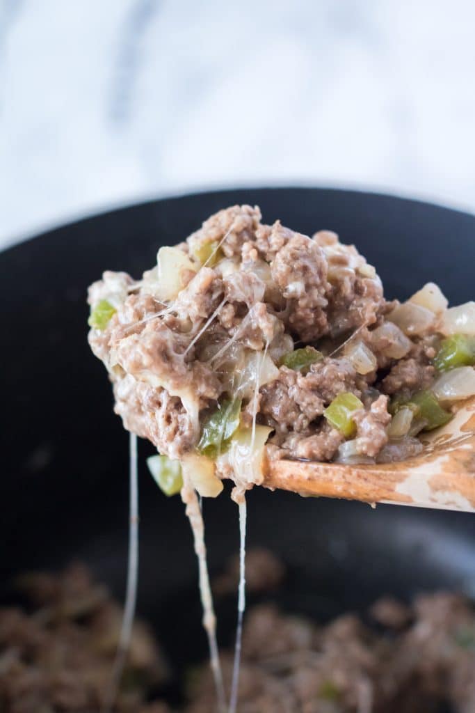 a wooden spoon holding up a scoop of slow cooker philly cheesesteak sloppy joe mixture