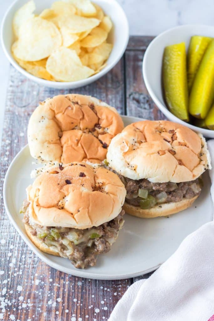 three slow cooker philly cheesesteak sloppy joes sandwiches on a white plate