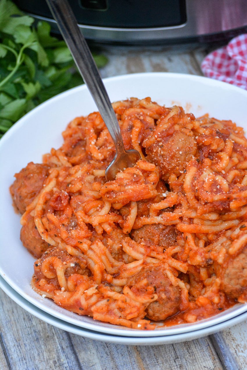a fork twirled in pasta - a white bowl of crockpot spaghetti and meatballs