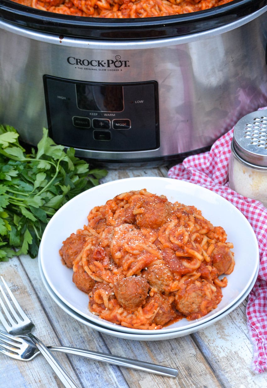 slow cooker spaghetti with meatballs in a white bowl in front of a crockpot