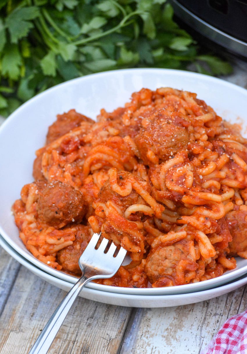 a fork twirled in pasta - a white bowl of crockpot spaghetti and meatballs
