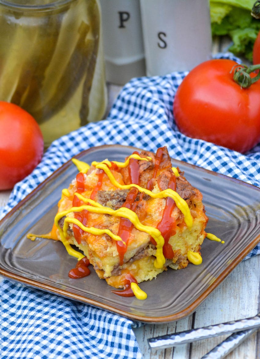 Cheeseburger Bread Pudding a slice of cheeseburger pudding drizzled with ketchup and mustard on a brown square plate