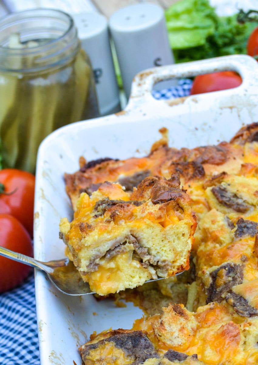 a silver spatula holding a slice of baked cheeseburger casserole above a white baking dish