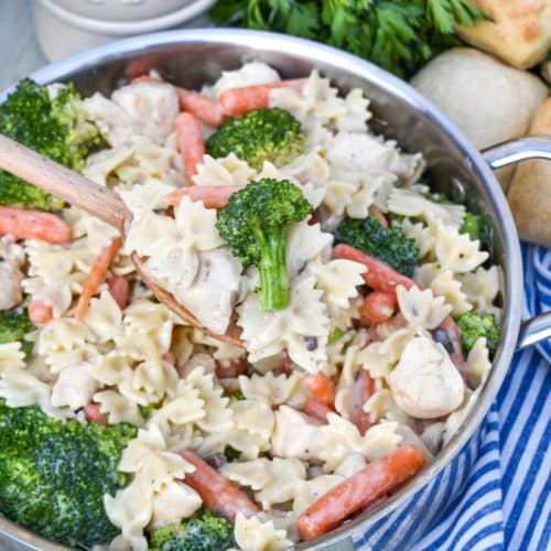 a wooden spoon holding up a scoop of creamy chicken pasta with broccoli and carrots