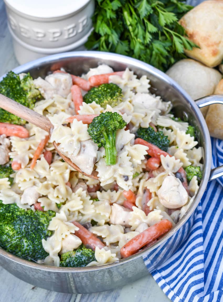 a wooden spoon holding up a scoop of creamy chicken pasta with broccoli and carrots
