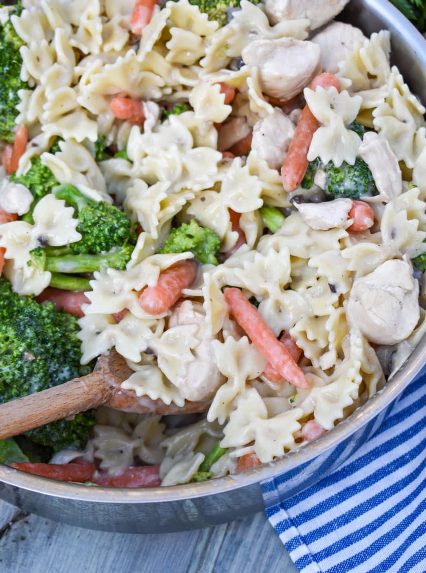 a wooden spoon in a pot of creamy chicken and bowties