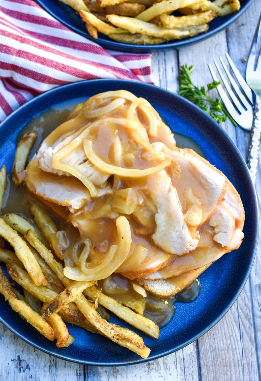 brown gravy covered open faced turkey sandwich on a blue plate with crispy fries on the side