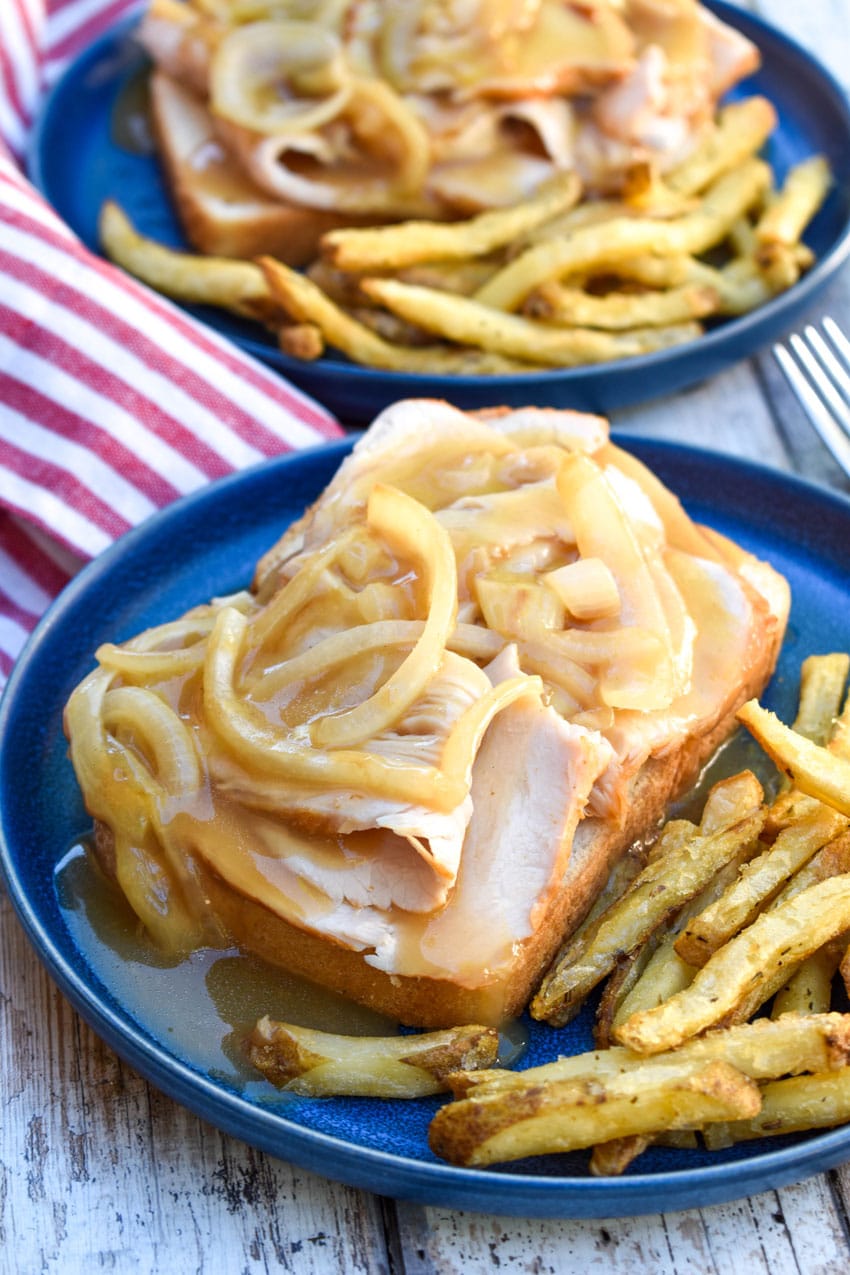 brown gravy covered open faced turkey sandwich on a blue plate with crispy fries on the side