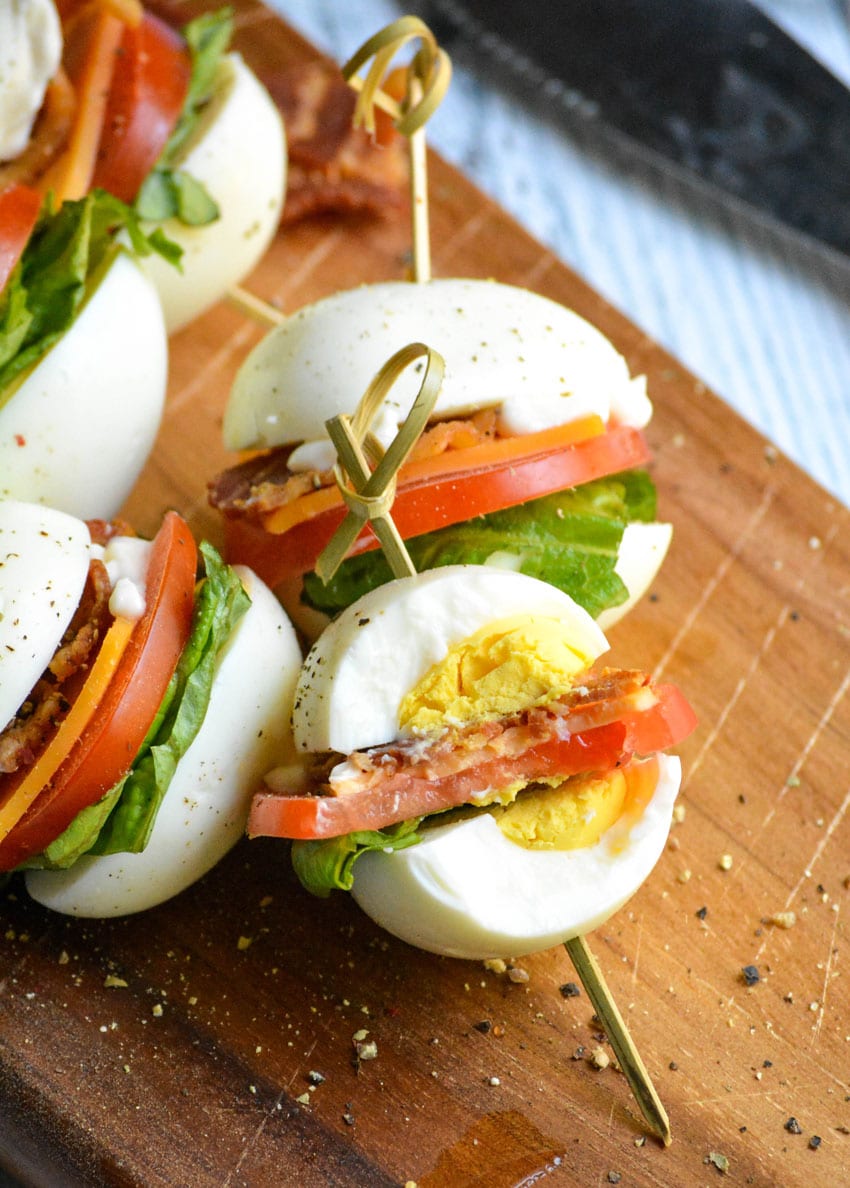 blt flavored hard boiled egg bites on toothpicks arranged on a wooden cutting board