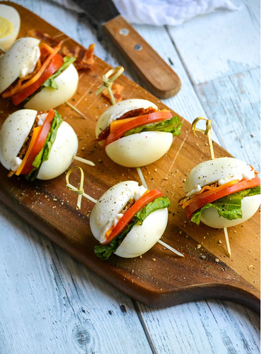 hard boiled egg blt bites arranged on a narrow wooden cutting board