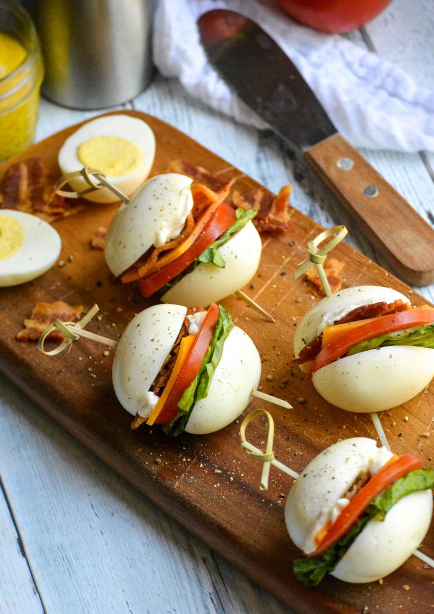 hard boiled egg blt bites arranged on a narrow wooden cutting board
