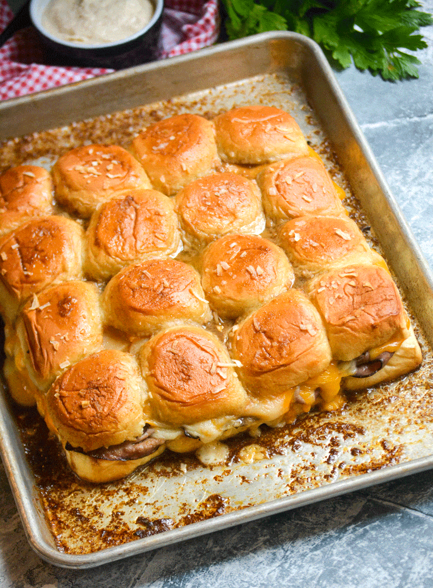 roast beef and cheddar sliders with horseradish sauce on a metal baking sheet