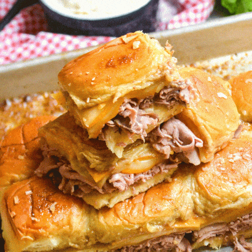 roast beef and cheddar sliders stacked on a metal baking sheet