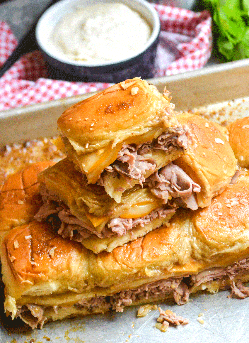 roast beef and cheddar sliders stacked on a metal baking sheet