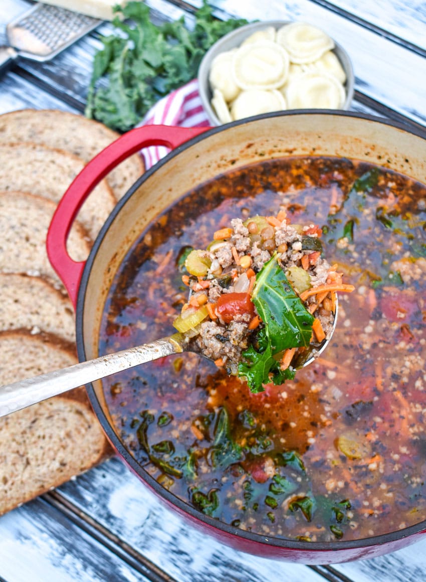 a silver ladle holding a scoop of sausage and lentil soup above a red Dutch oven