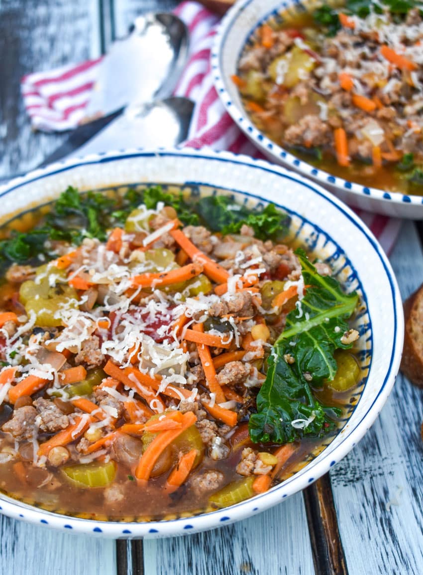 two bowls of easy sausage and lentil soup on a wooden table