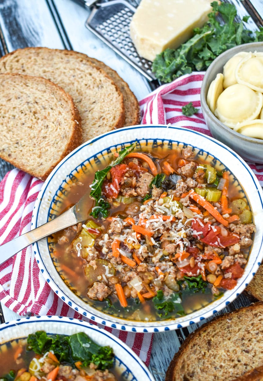 a silver spoon in a bowl of sausage and lentil soup with kale
