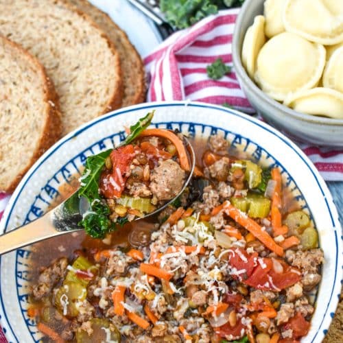 a silver spoon in a bowl of sausage and lentil soup with kale