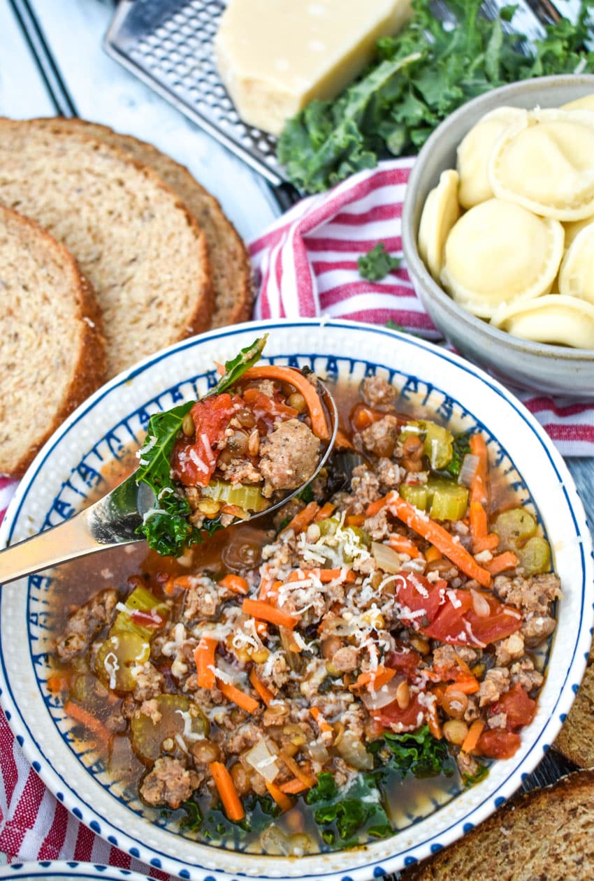 a silver spoon in a bowl of sausage and lentil soup with kale