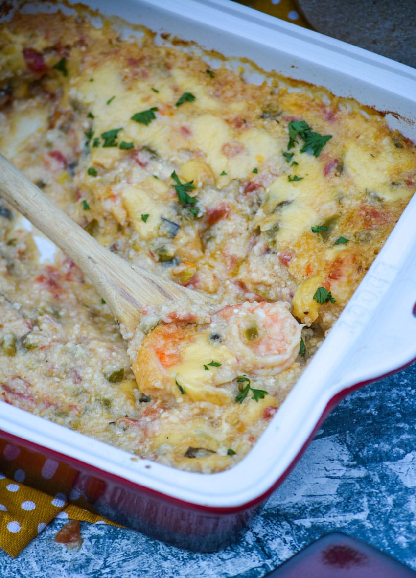 a wooden spoon stuck in a shrimp and grits casserole dish