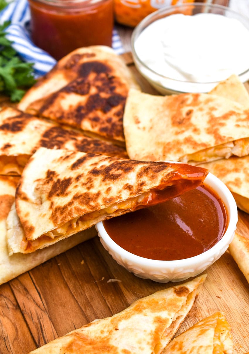 a cheesy chicken quesadilla resting on a small white bowl of mild taco sauce