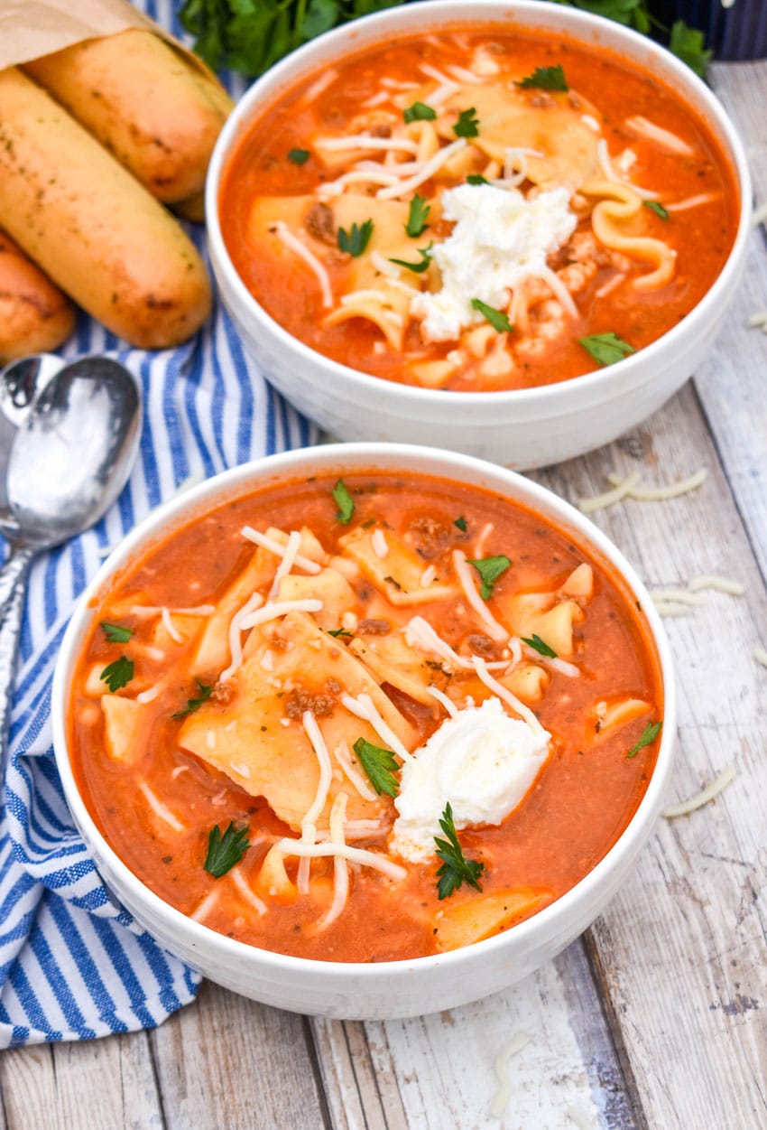easy lasagna soup in two white bowls topped with dollops of ricotta cheese and fresh herbs