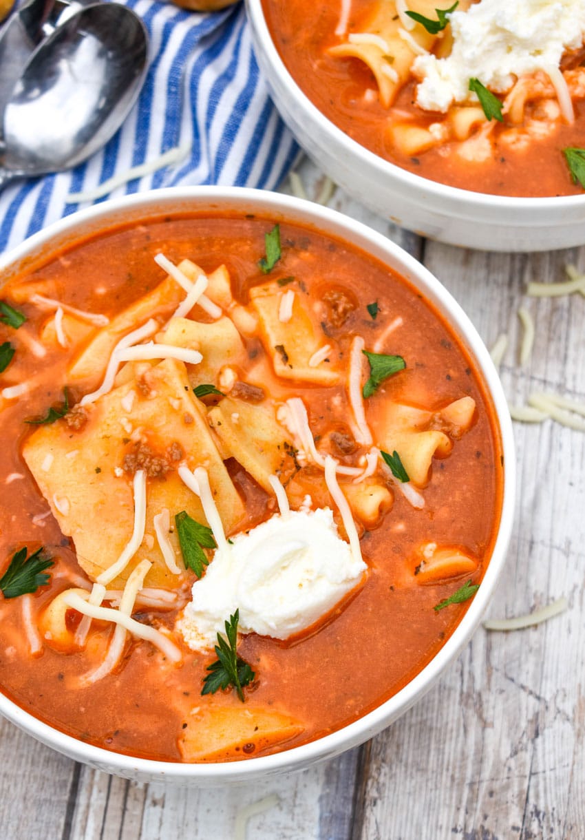 easy lasagna soup in two white bowls topped with dollops of ricotta cheese and fresh herbs