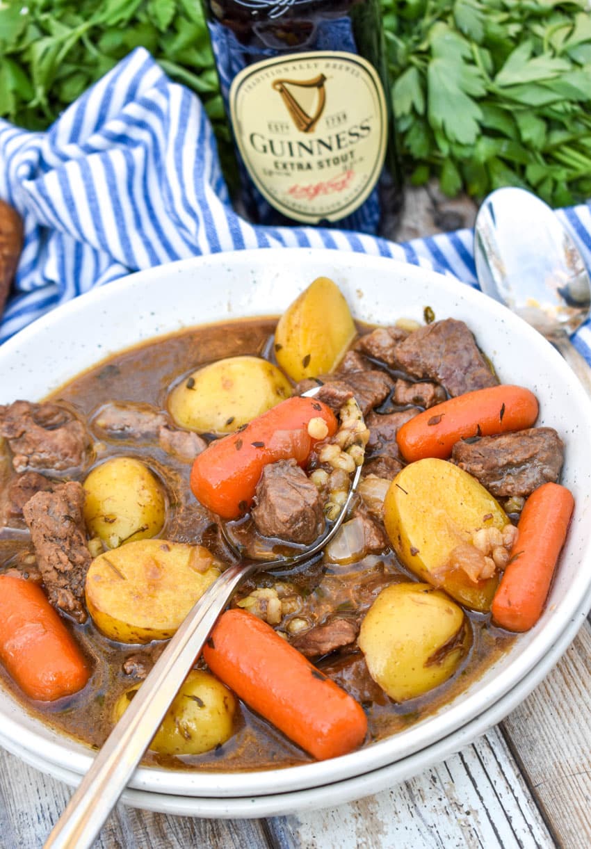 a silver spoon in a white bowl filled with guinness beef stew