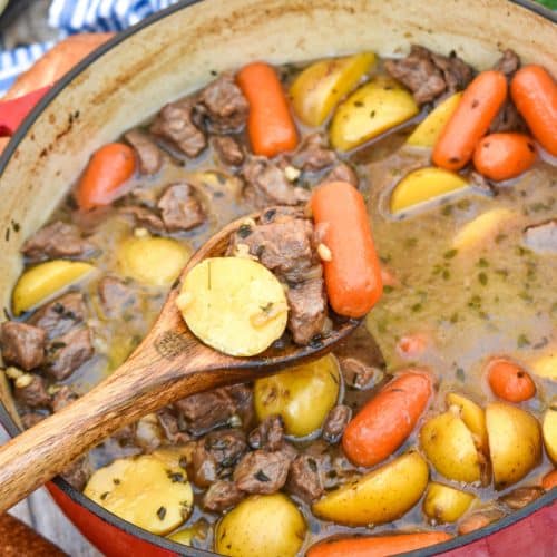 a wooden spoon with a scoop of slow cooker guinness beef stew above a red pot