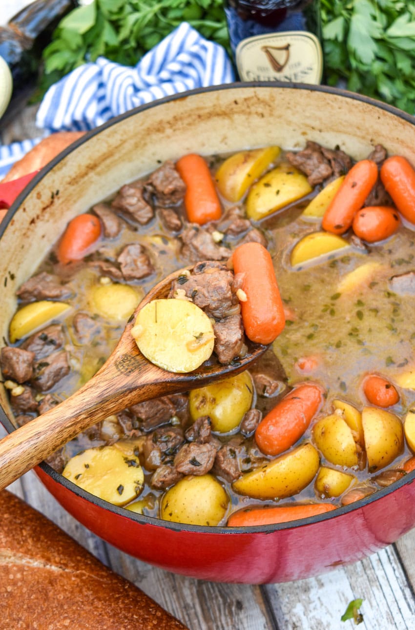 a wooden spoon with a scoop of slow cooker guinness beef stew above a red pot