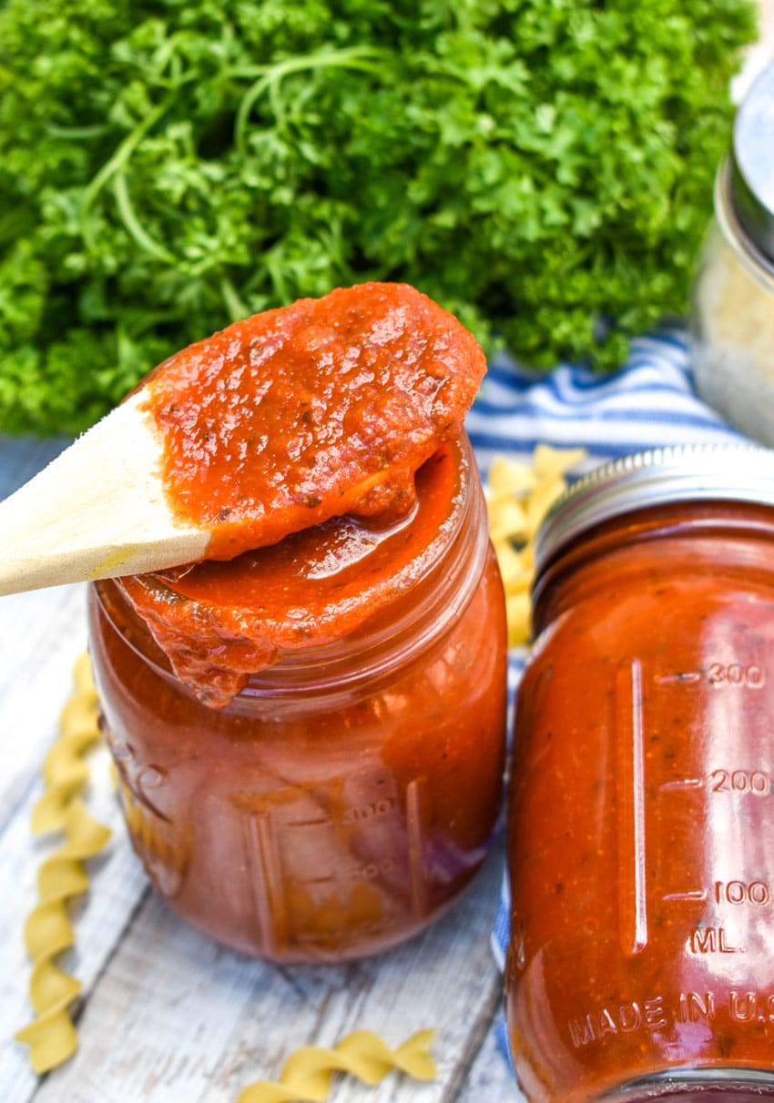 a wooden spoon holding doctored canned tomato sauce resting on a glass jar