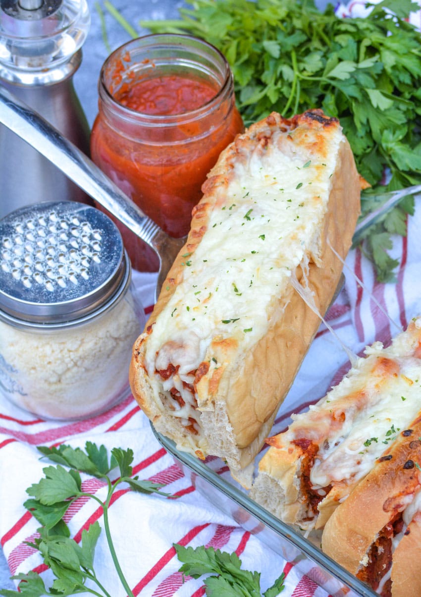 a silver spatula lifting a baked meatball sub out of a glass baking dish