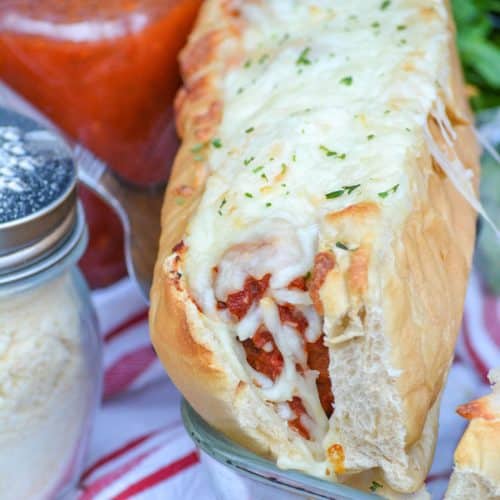 a silver spatula lifting a baked meatball sub out of a glass baking dish