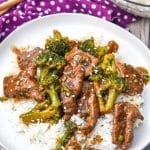 slow cooker beef and broccoli over steamed white rice on a white plate