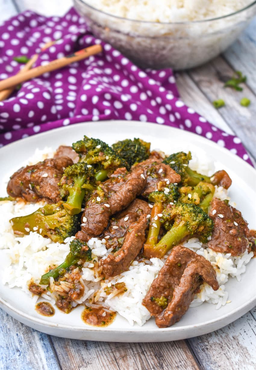 slow cooker beef and broccoli over steamed white rice on a white plate