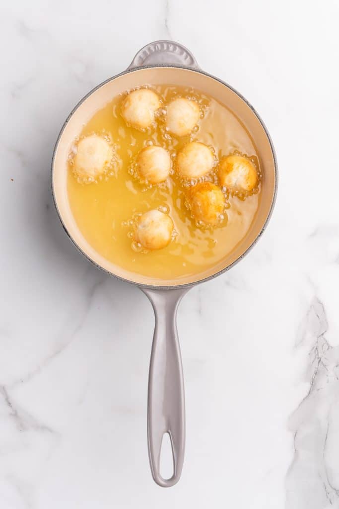 balls of biscuit dough frying in oil in a gray skillet