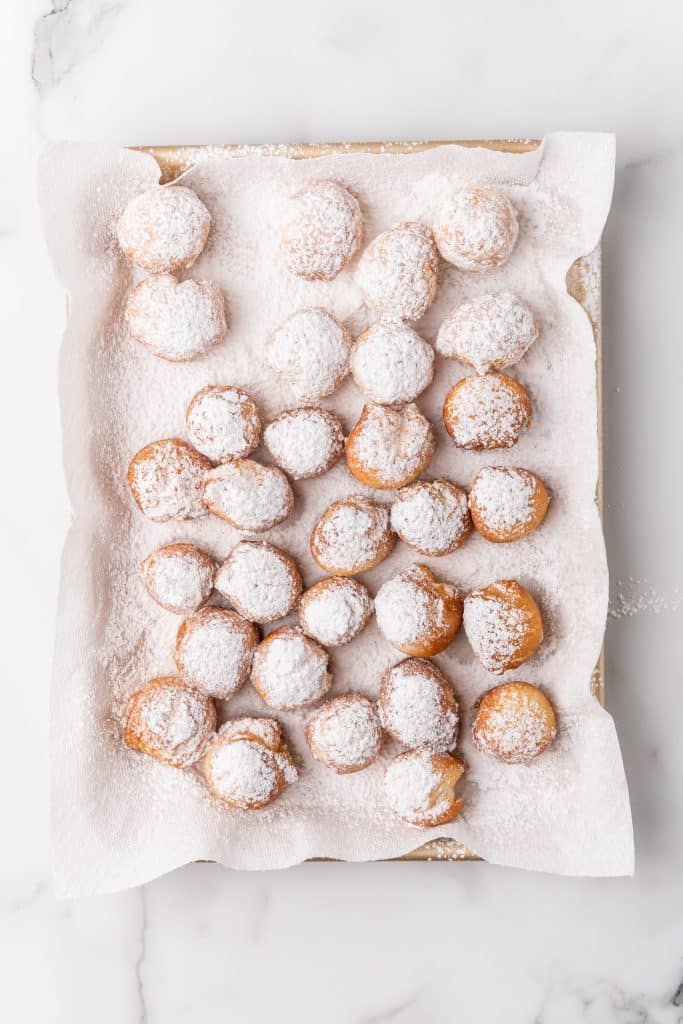 powdered sugar coated beignets on a paper towel lined baking pan