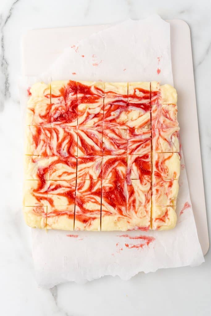 strawberry fudge cut into squares on a white cutting board