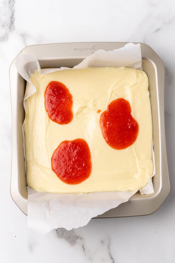 strawberry sauce topped white chocolate fudge in a parchment paper lined baking dish