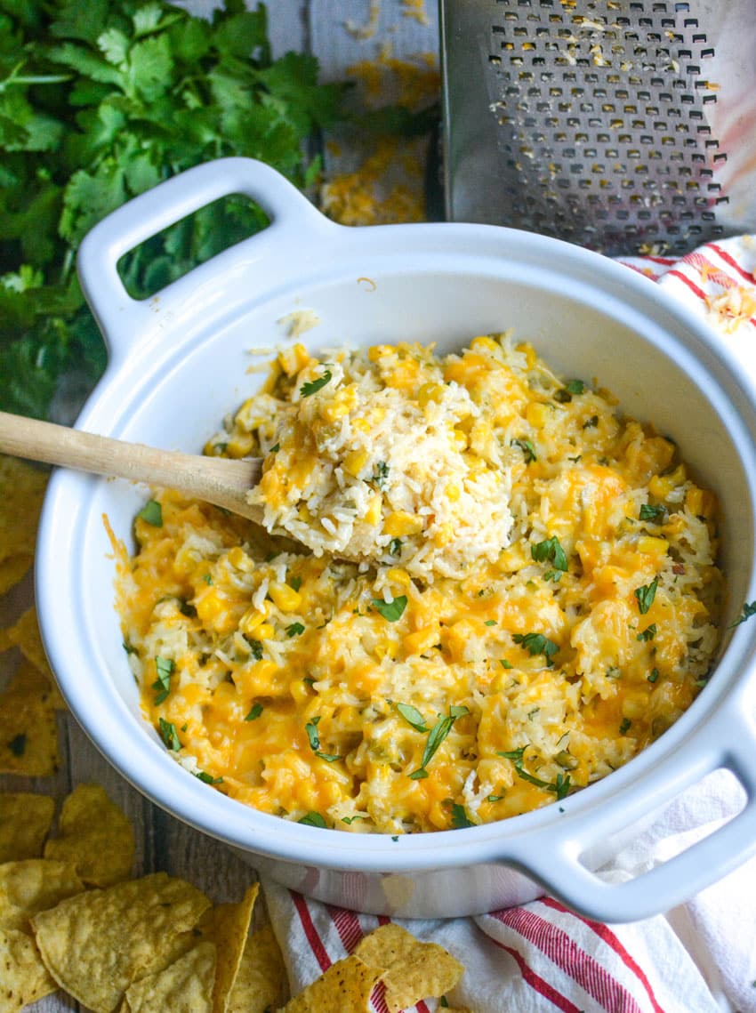 a wooden spoon in a white bowl filled with cheesy cilantro and sour cream rice