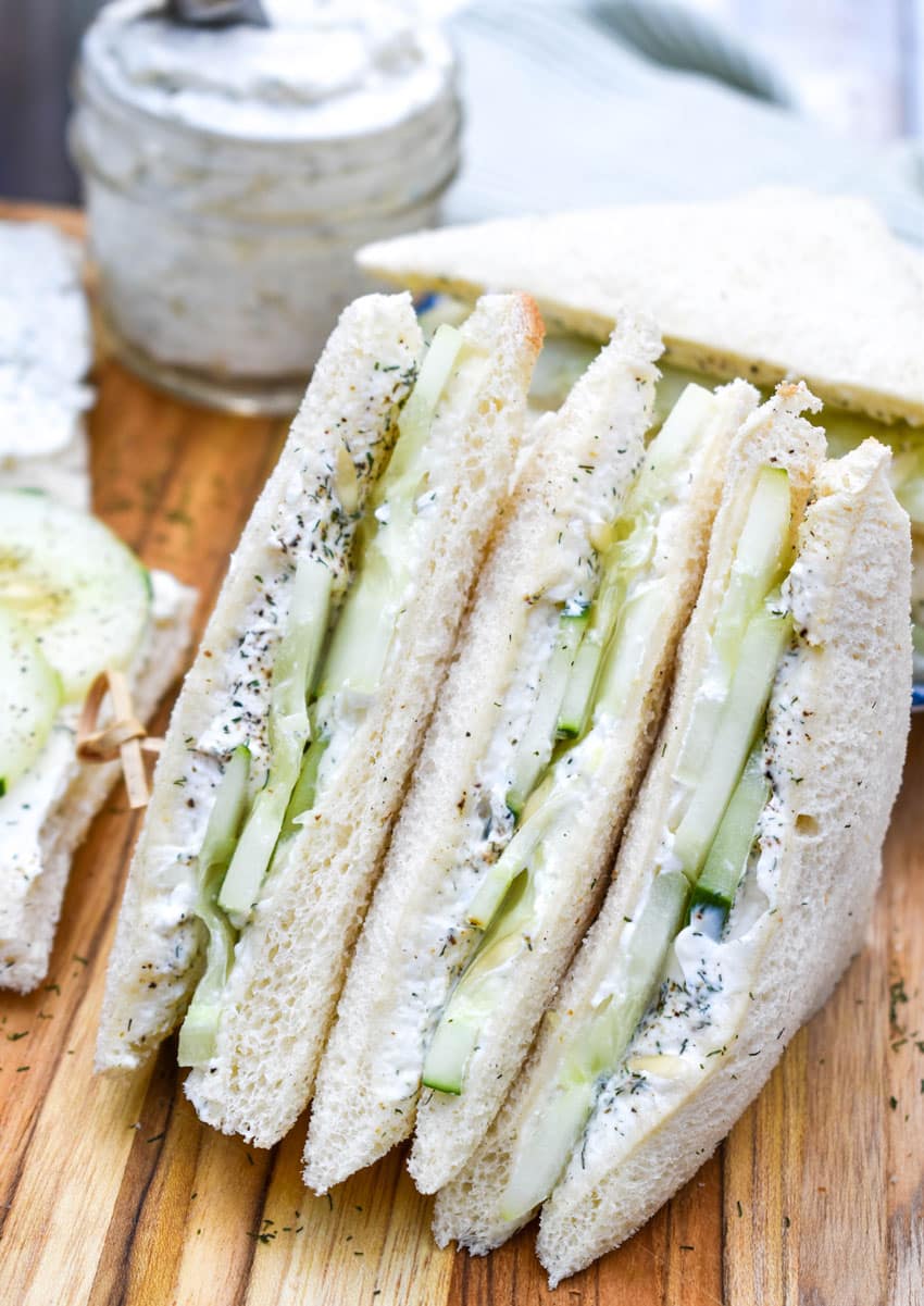 a row of cucumber tea sandwiches cut into triangles on a wooden plate