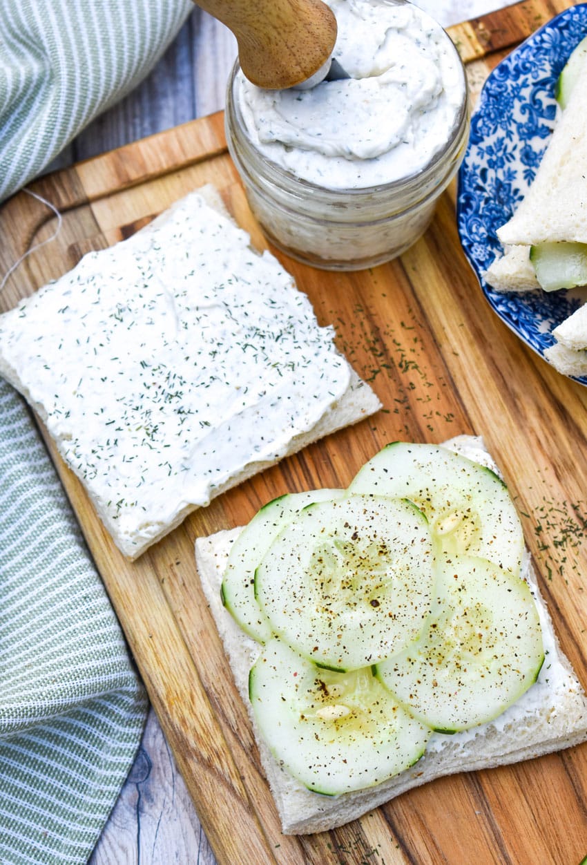 an open cucumber tea sandwich on a wooden cutting board