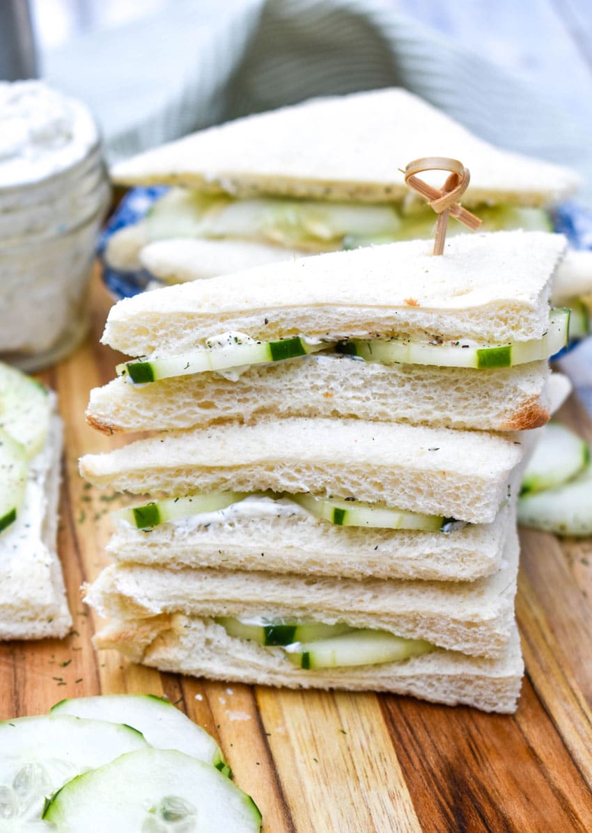 a stack of cucumber tea sandwiches on a wooden cutting board