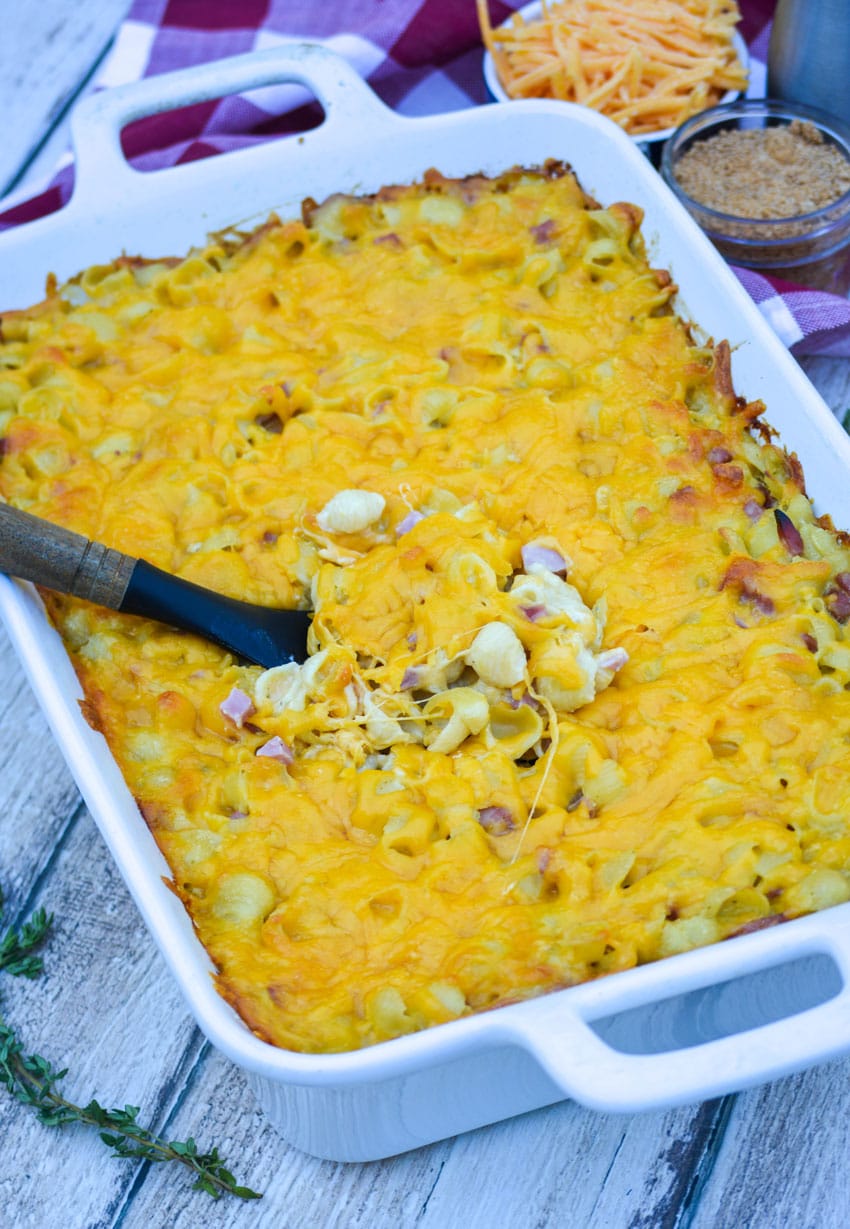 a serving spoon scooping cheesy baked macaroni out of a white baking dish